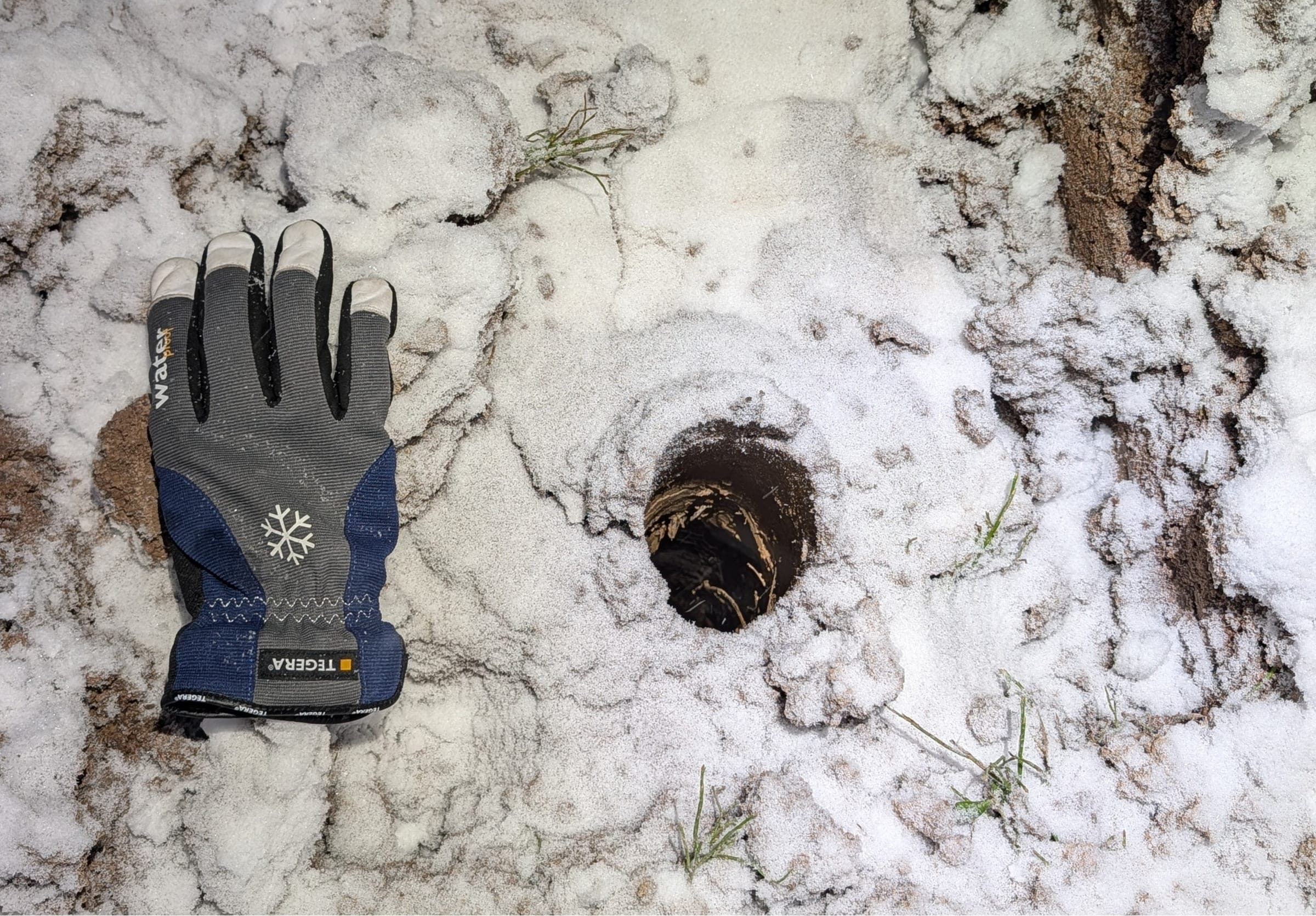A small sampling hole in frosty ground, with a work glove beside it for scale.